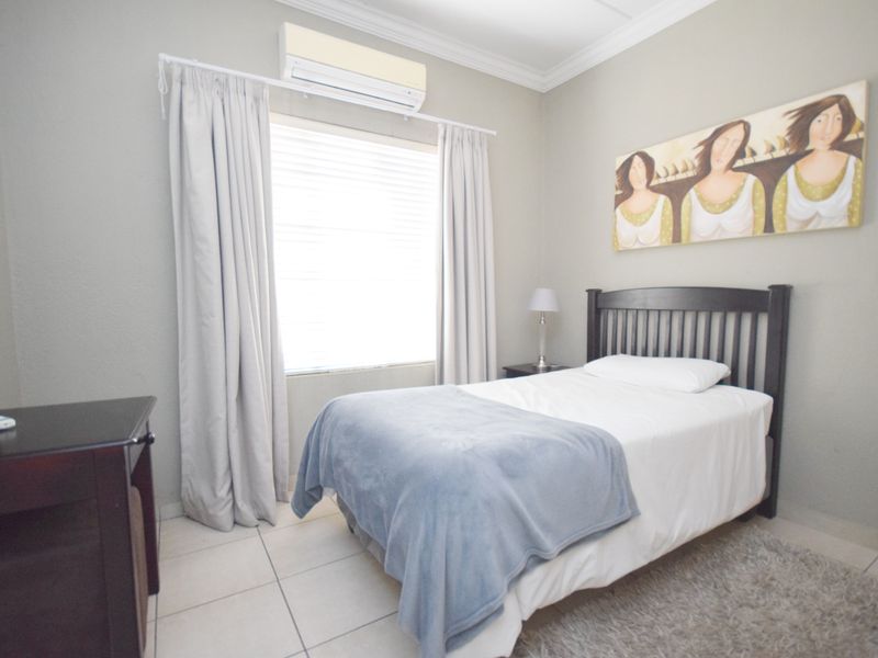 A well-maintained bedroom featuring neutral wall tones, tiled flooring, and a wall-mounted split-system air conditioning unit.