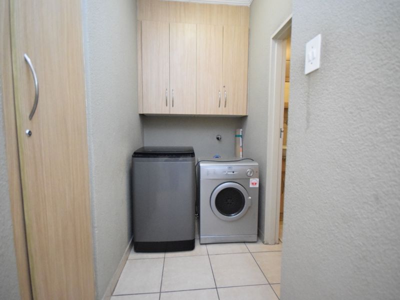 A functional laundry area featuring built-in overhead cabinetry and tiled flooring with dedicated plumbing connections for appliances.