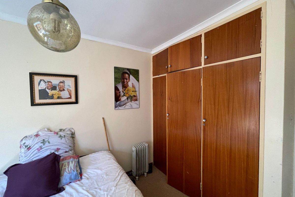 A bedroom featuring built-in wooden wardrobes with overhead storage cupboards and a pendant light fixture.