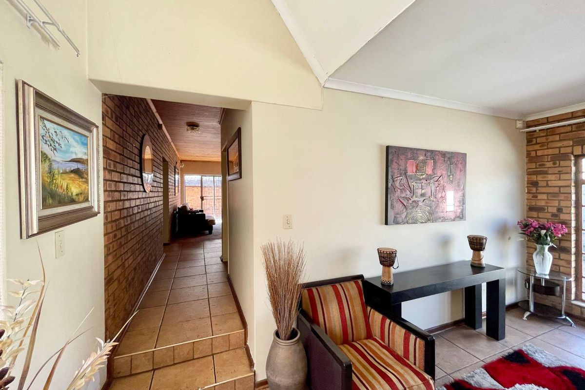 A view from the living area into a hallway featuring exposed brick walls, tiled flooring, and a vaulted ceiling.