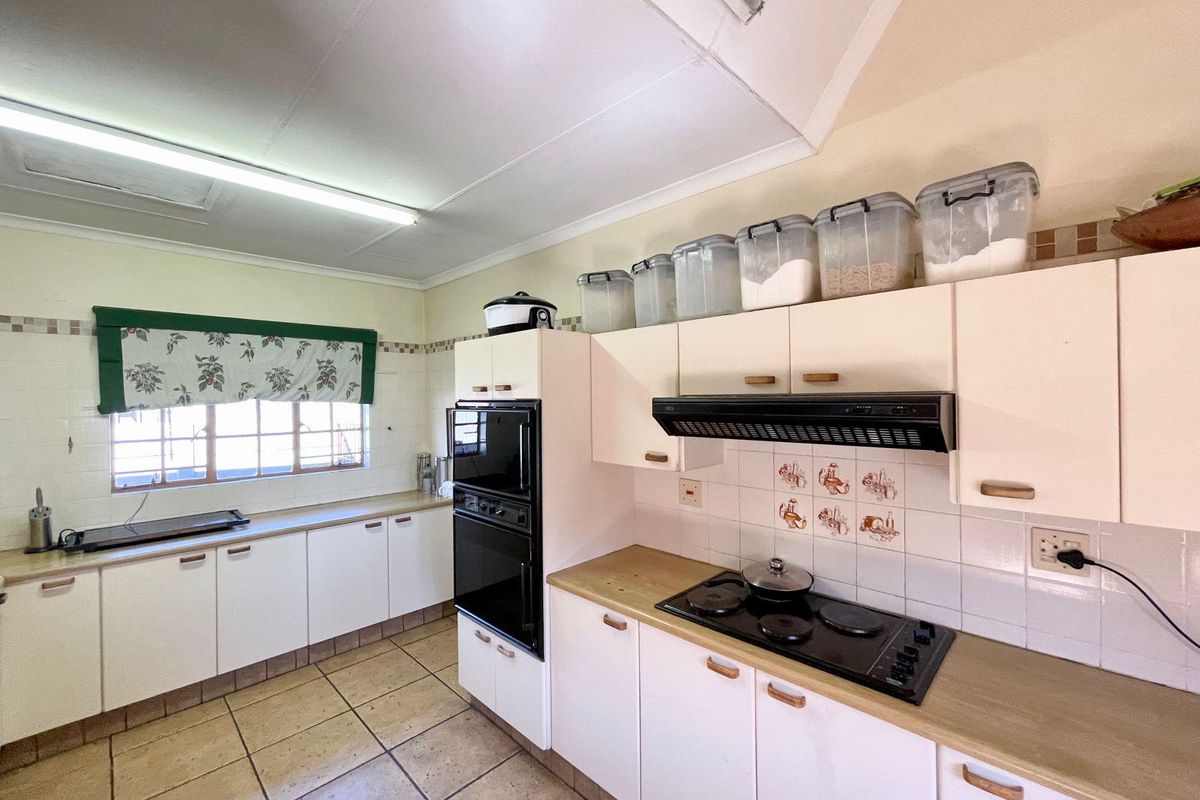 A functional kitchen featuring built-in cabinetry, a wall-mounted oven, a hob with an extractor fan, and tiled flooring.