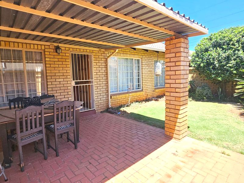 Covered outdoor patio area featuring brick paving and a sturdy brick pillar, providing a functional space for outdoor dining overlooking the garden.