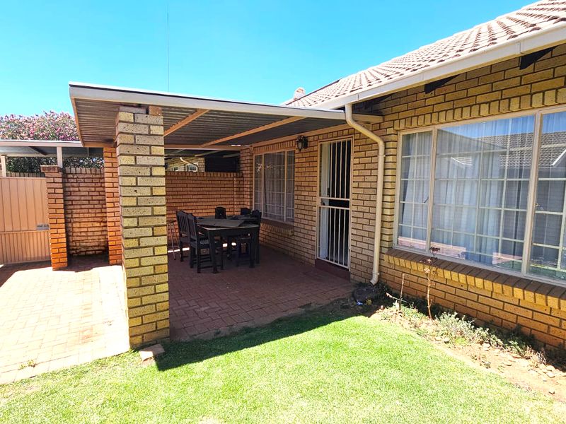 A covered brick patio area featuring paved flooring and a security gate, providing a functional outdoor space adjacent to the main townhouse structure.