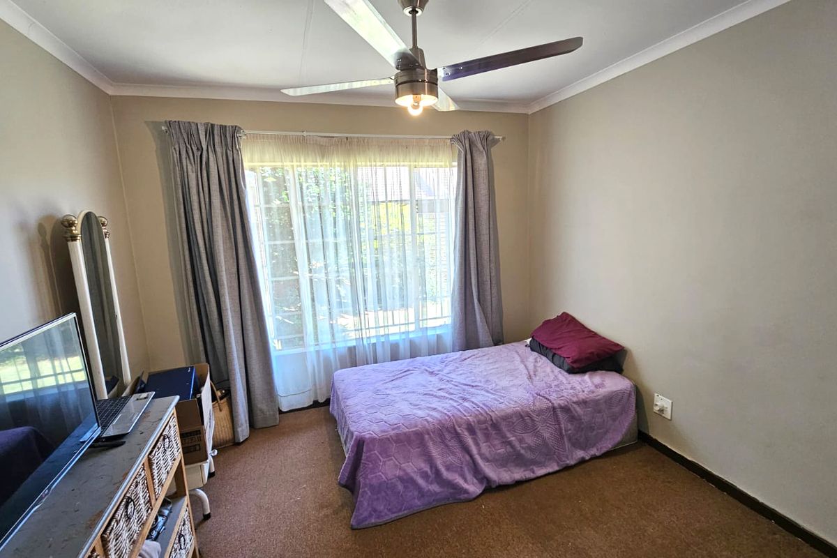 A functional bedroom featuring a ceiling fan, carpeted flooring, and large windows with curtains, providing a comfortable and well-lit living space.