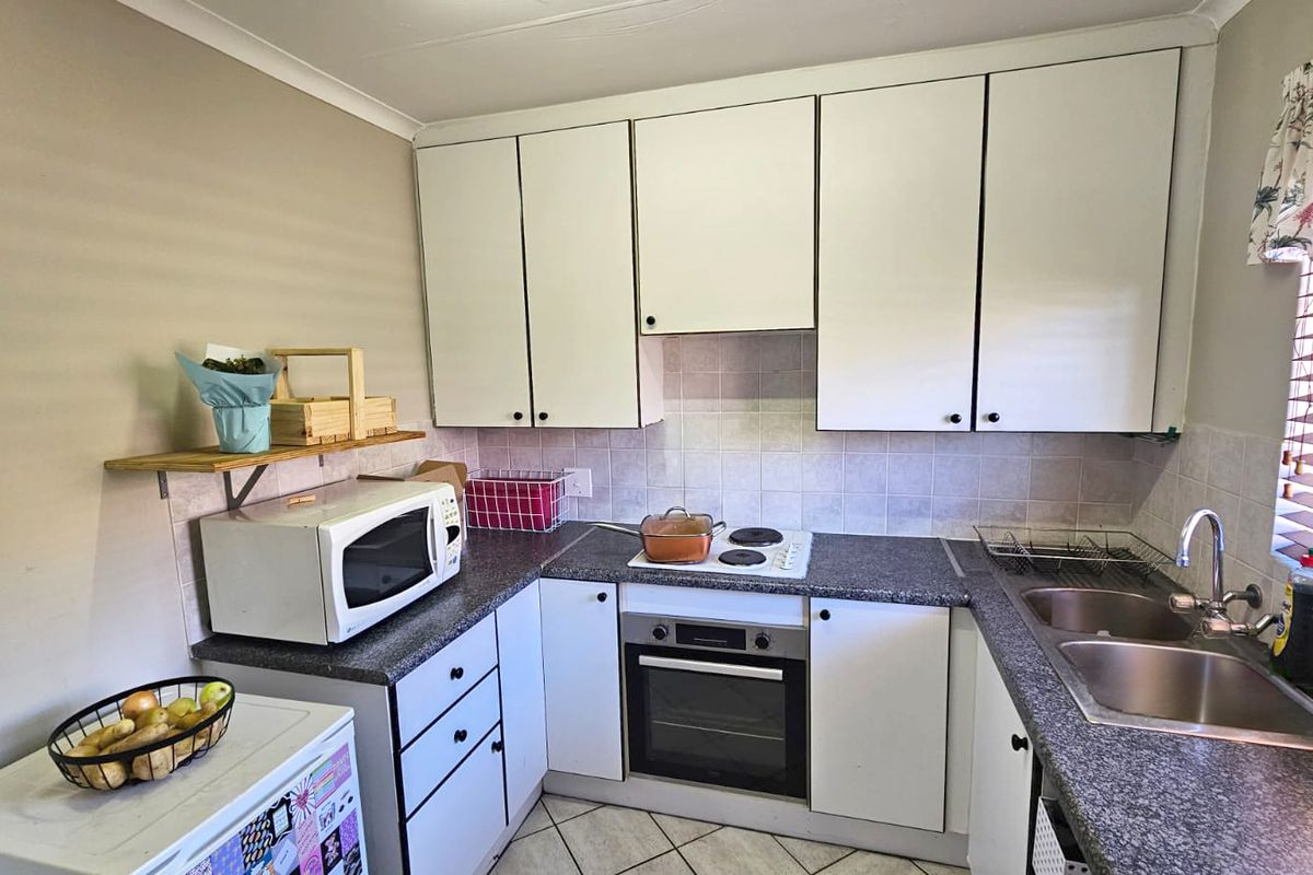 A functional kitchen featuring white cabinetry, laminate countertops, a built-in oven with electric hob, and a double stainless steel sink with tiled splashback.