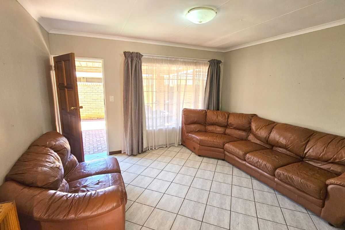 A spacious living room featuring neutral tiled flooring, cove ceiling detailing, and direct access to an outdoor patio area through a timber door.