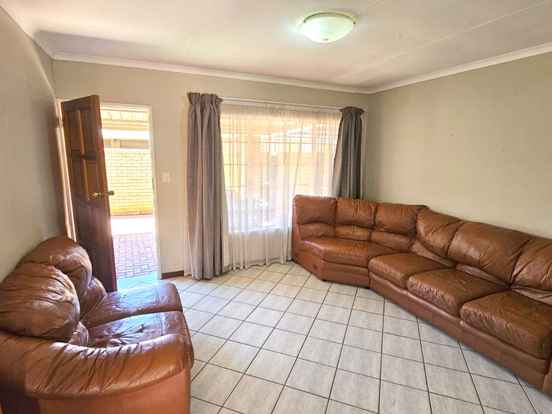 A spacious living room featuring neutral tiled flooring, cove ceiling detailing, and direct access to an outdoor patio area through a timber door.