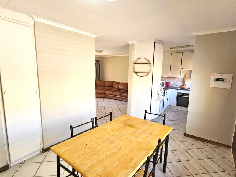 Open-plan living and dining area featuring tiled flooring, built-in kitchen cabinetry with integrated oven and hob, and neutral wall finishes.
