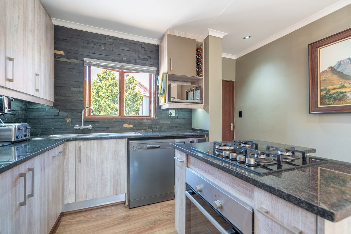 Modern kitchen featuring granite countertops, stone veneer backsplash, built-in gas hob, oven, and integrated dishwasher with light wood cabinetry.