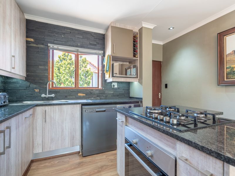 Modern kitchen featuring granite countertops, stone veneer backsplash, built-in gas hob, oven, and integrated dishwasher with light wood cabinetry.