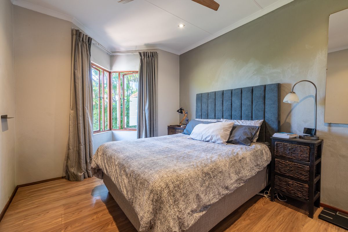 A well-lit bedroom featuring laminate flooring, a ceiling fan, and a bay window that provides natural light.