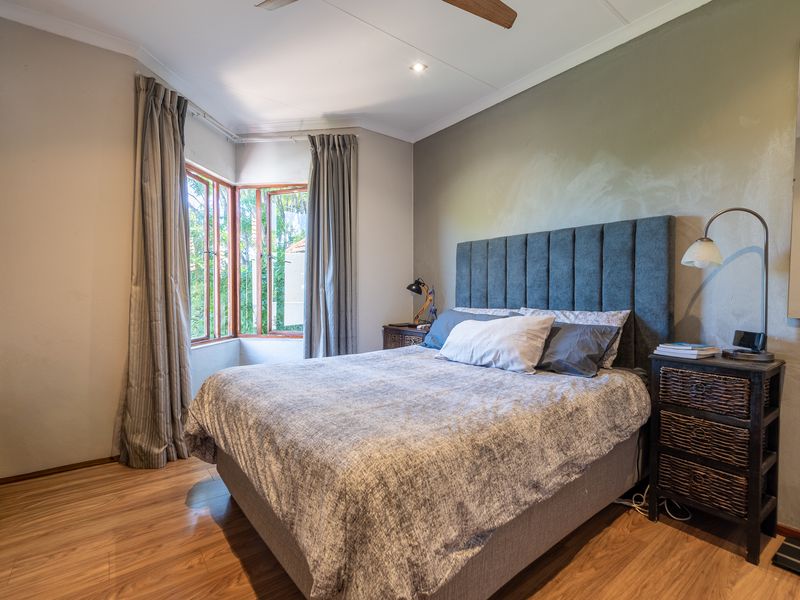 A well-lit bedroom featuring laminate flooring, a ceiling fan, and a bay window that provides natural light.