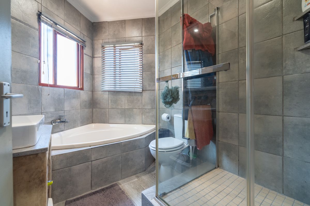 A functional bathroom featuring a corner bathtub, a separate glass-enclosed shower, and grey wall tiling throughout.