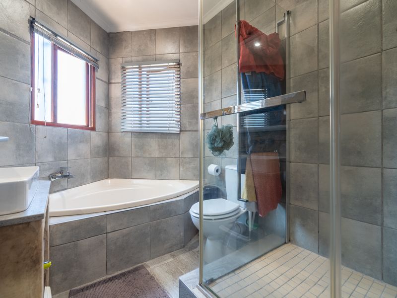 A functional bathroom featuring a corner bathtub, a separate glass-enclosed shower, and grey wall tiling throughout.