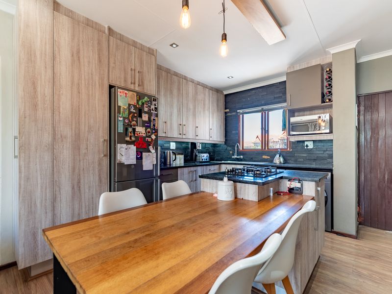 Modern open-plan kitchen featuring wood-grain cabinetry, stone countertops, a gas hob, and an integrated breakfast bar, creating a functional and stylish living space.