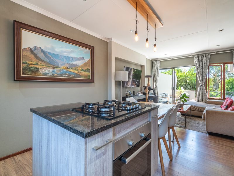 Modern open-plan living area featuring a kitchen island with gas hob, built-in oven, granite countertops, and seamless flow to the outdoor patio area.