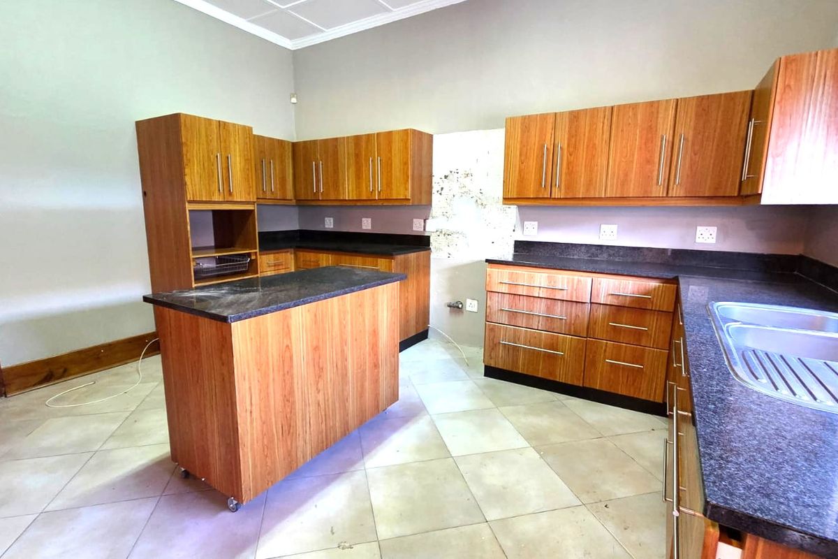 A spacious kitchen featuring wood-look cabinetry, granite countertops, a central island, and tiled flooring, requiring minor cosmetic repairs to the wall finish.