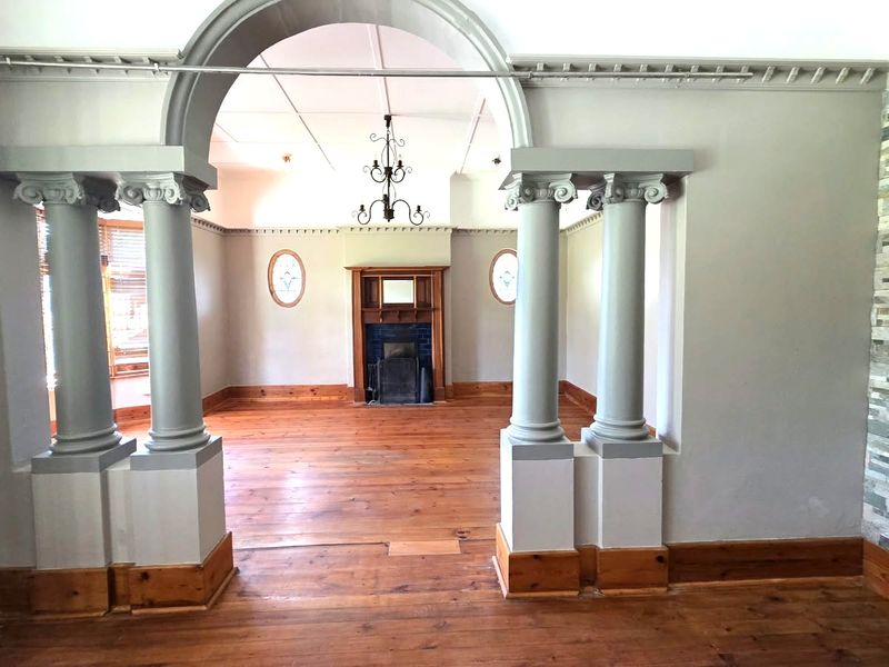 Spacious living area featuring an elegant arched entryway with decorative columns, hardwood flooring, a fireplace, and a striking stone feature wall.