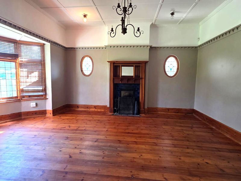 Spacious living room featuring original timber flooring, a classic fireplace with a timber mantel, bay window, and decorative period ceiling details.