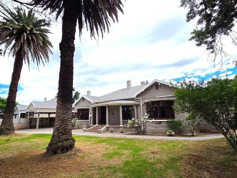 Front elevation of a traditional house featuring a covered porch, established palm trees, and a spacious front garden with a concrete driveway.