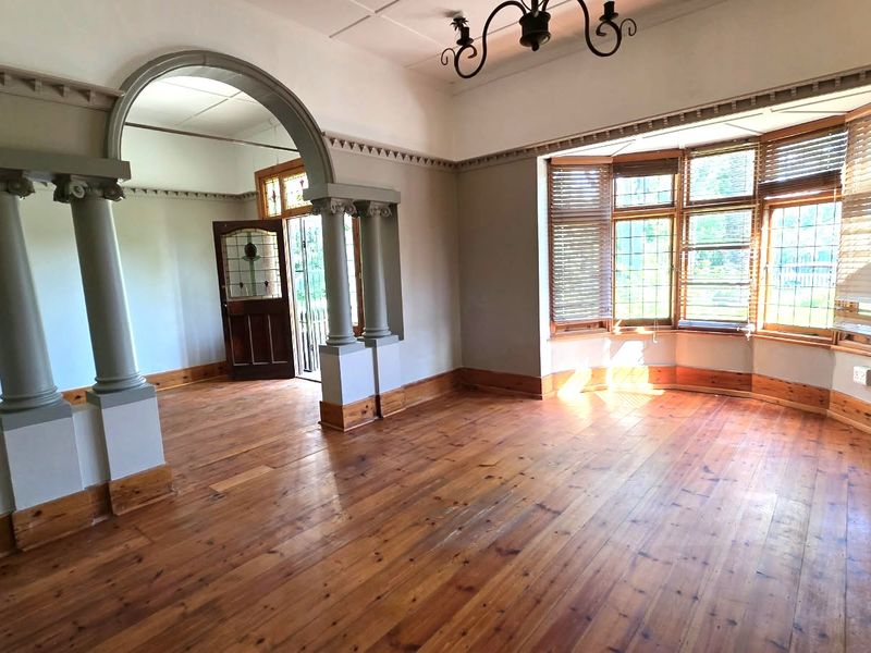 Spacious living area featuring original hardwood flooring, a classic bay window, and an elegant arched entryway with decorative columns.