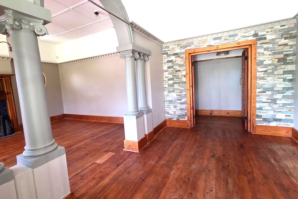 Spacious living area featuring original hardwood floors, decorative columns, a stone veneer feature wall, and a classic fireplace, offering a character-filled blank canvas.