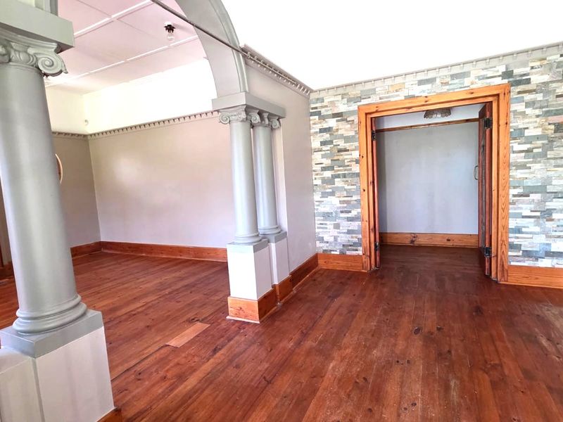 Spacious living area featuring original hardwood floors, decorative columns, a stone veneer feature wall, and a classic fireplace, offering a character-filled blank canvas.