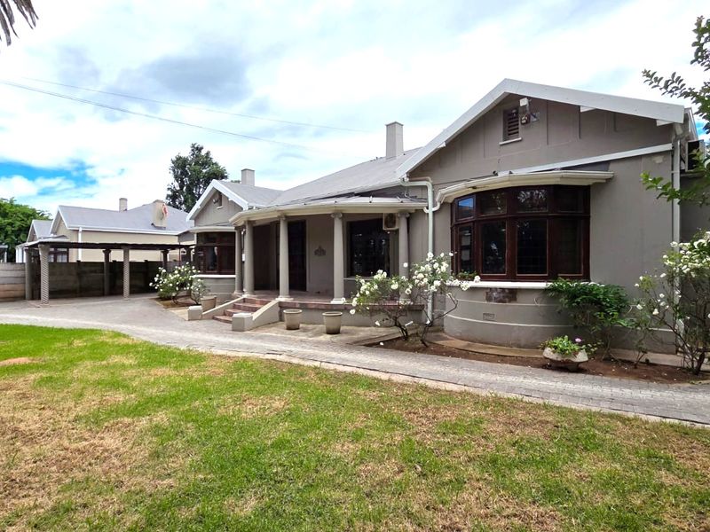 A well-maintained single-story house featuring a covered porch with classical columns, a bay window, and a paved driveway leading to a carport.