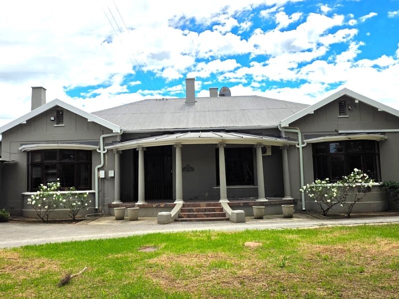A well-maintained single-story residence featuring a covered veranda with classical columns, bay windows, and a paved driveway set within a landscaped garden.