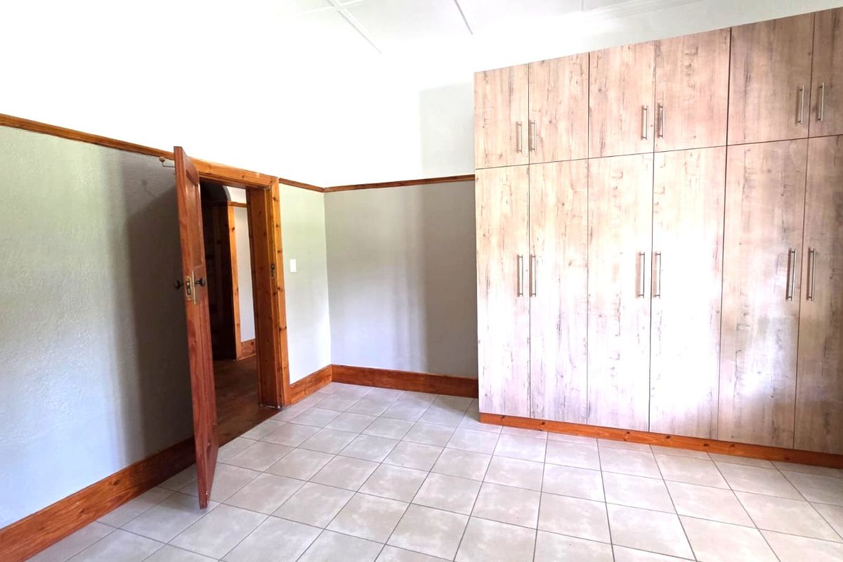 A spacious bedroom featuring neutral tiled flooring, extensive built-in wooden cupboards, and classic wooden trim detailing throughout.