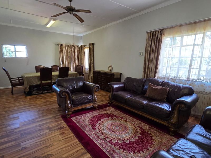 Spacious open-plan living and dining area featuring laminate flooring, a ceiling fan, and large windows with security bars.