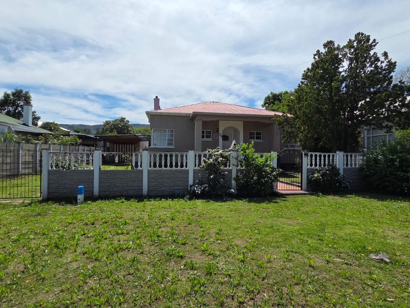 Front view of a single-story house featuring a covered porch, corrugated metal roof, and a fenced front garden with a metal gate.