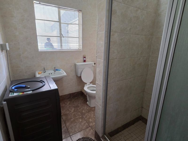 A functional bathroom featuring a shower enclosure, pedestal basin, and toilet, finished with neutral wall and floor tiling.