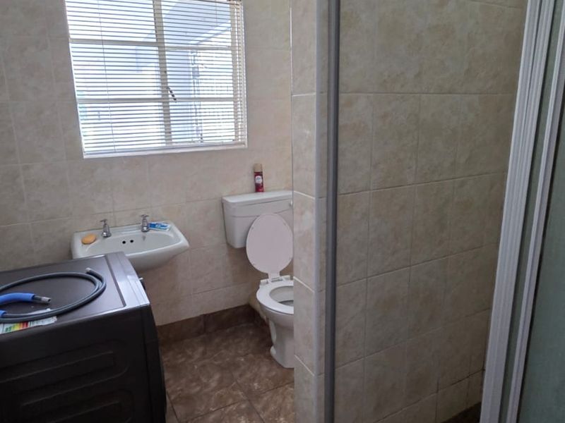 A functional bathroom featuring a shower enclosure, toilet, and wall-mounted basin with neutral tiled finishes throughout.