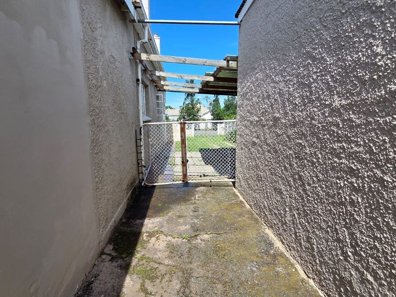 A narrow side passage featuring a concrete walkway, a chain-link gate, and a weathered timber pergola structure leading to the rear garden area.