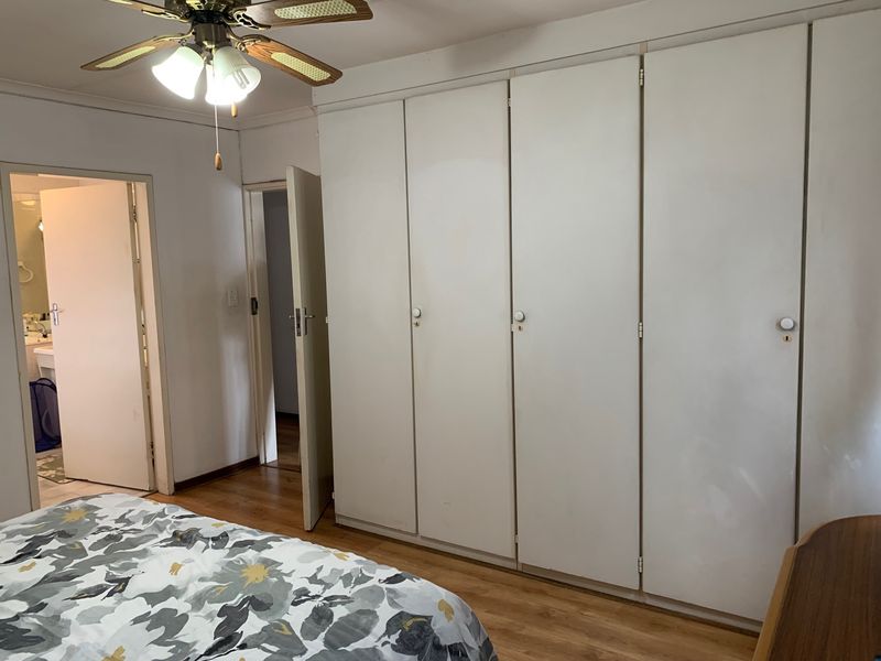 A bedroom featuring laminate flooring, a ceiling fan, and extensive built-in cupboard storage, with direct access to an adjoining bathroom.