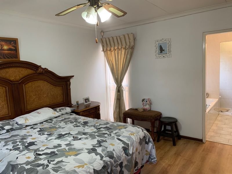 A well-lit bedroom featuring laminate flooring, a ceiling fan, and direct access to an en-suite bathroom.