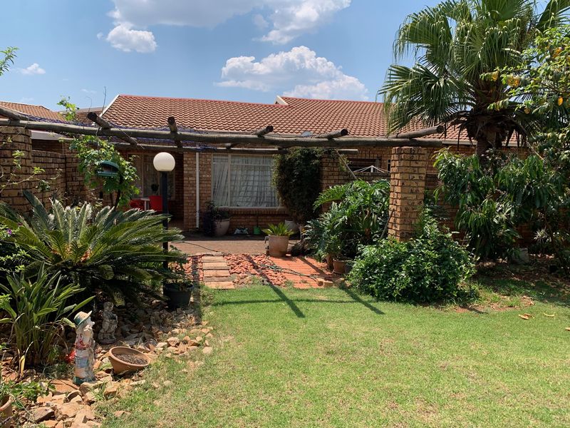 Rear view of the townhouse featuring a brick facade, tiled roof, and a timber pergola over a paved patio area with a landscaped garden.