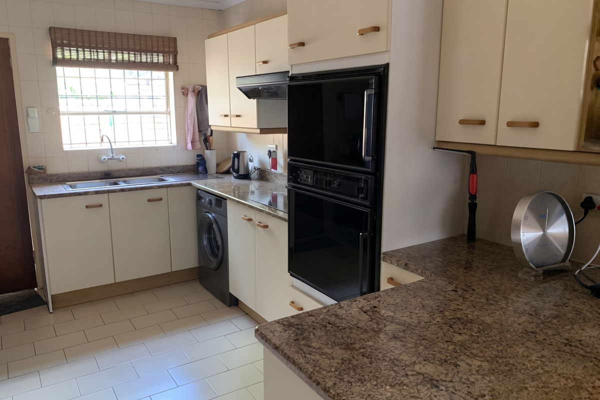A functional kitchen featuring granite countertops, built-in cabinetry, a double sink, and integrated oven with extractor fan, finished with tiled flooring and backsplash.