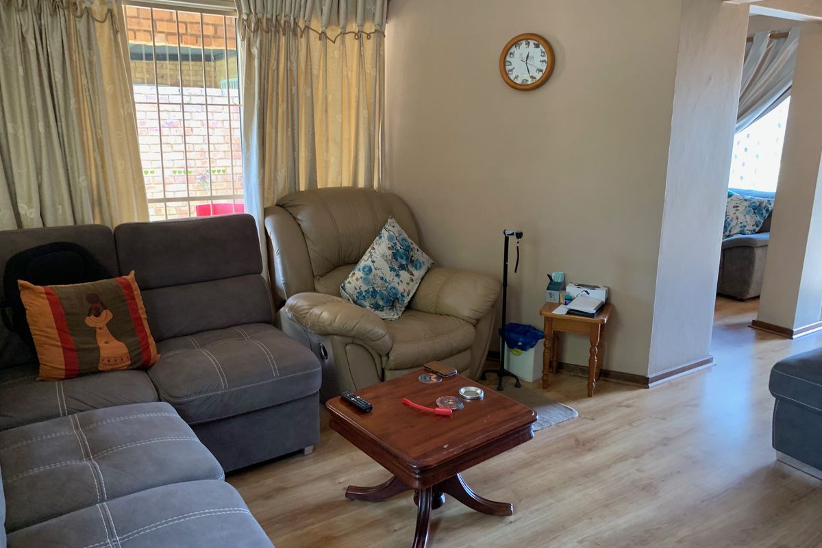 A comfortable living room featuring laminate flooring and a window with security bars, offering a functional and lived-in space.