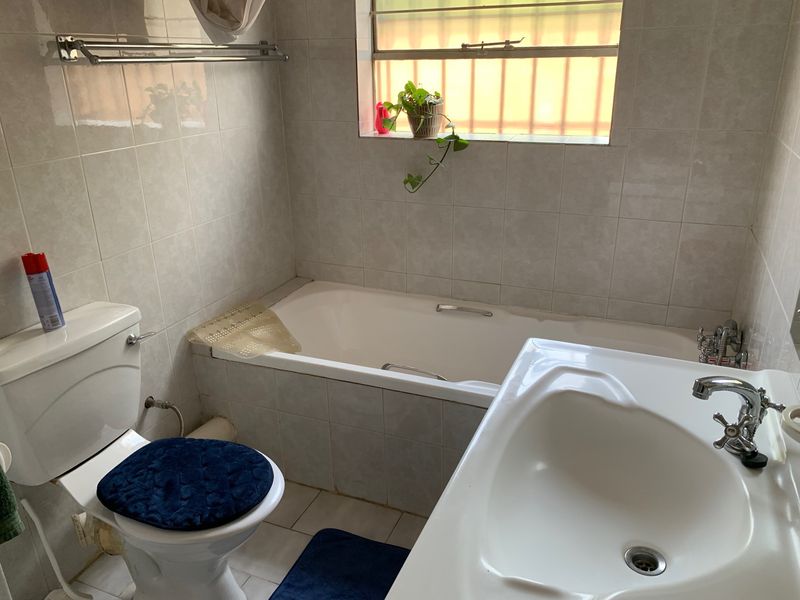 A functional bathroom featuring a built-in bathtub, pedestal washbasin, and toilet, finished with neutral ceramic wall and floor tiles.