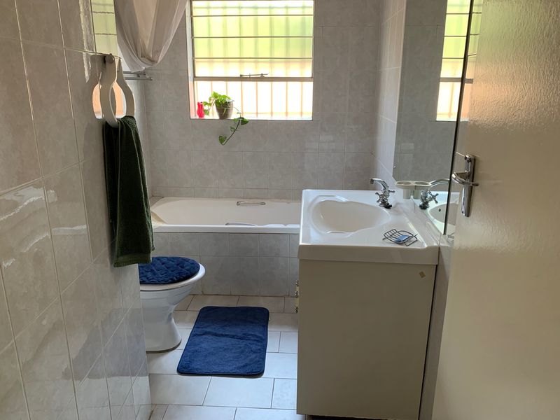 A functional bathroom featuring a built-in bathtub, vanity cabinet with washbasin, and fully tiled walls and floors.