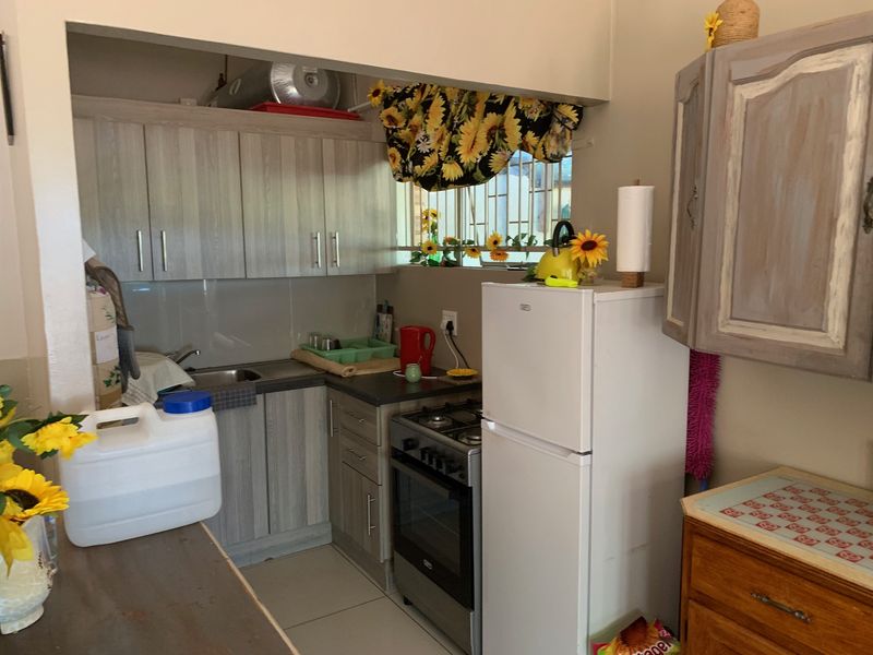 Compact kitchen featuring built-in cabinetry, stainless steel sink, gas stove with oven, and tiled splashback, offering a functional layout for a cottage.