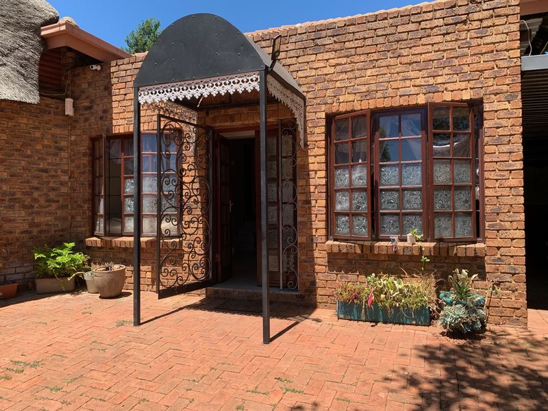 A charming cottage exterior featuring exposed brick walls, a decorative wrought iron security gate, a metal entrance canopy, and a brick-paved patio area.