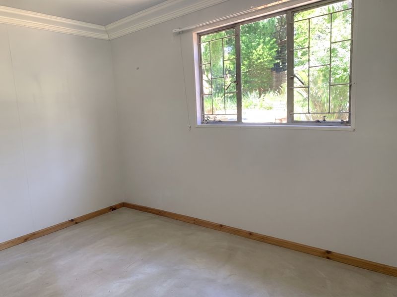 A bright, empty bedroom featuring neutral walls, timber skirting boards, and a window fitted with metal security bars.