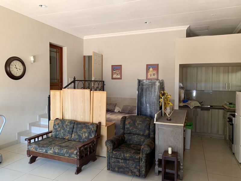 Open-plan living area featuring tiled floors, recessed lighting, and a compact kitchen with built-in cabinetry, seamlessly connected to a staircase leading to upper levels.