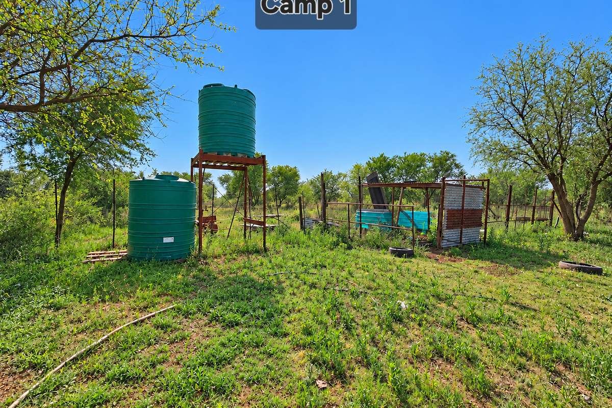 Outdoor farm area featuring two large water storage tanks on a metal stand and a small corrugated metal shelter structure.