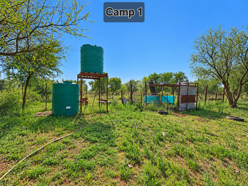 Outdoor farm area featuring two large water storage tanks on a metal stand and a small corrugated metal shelter structure.