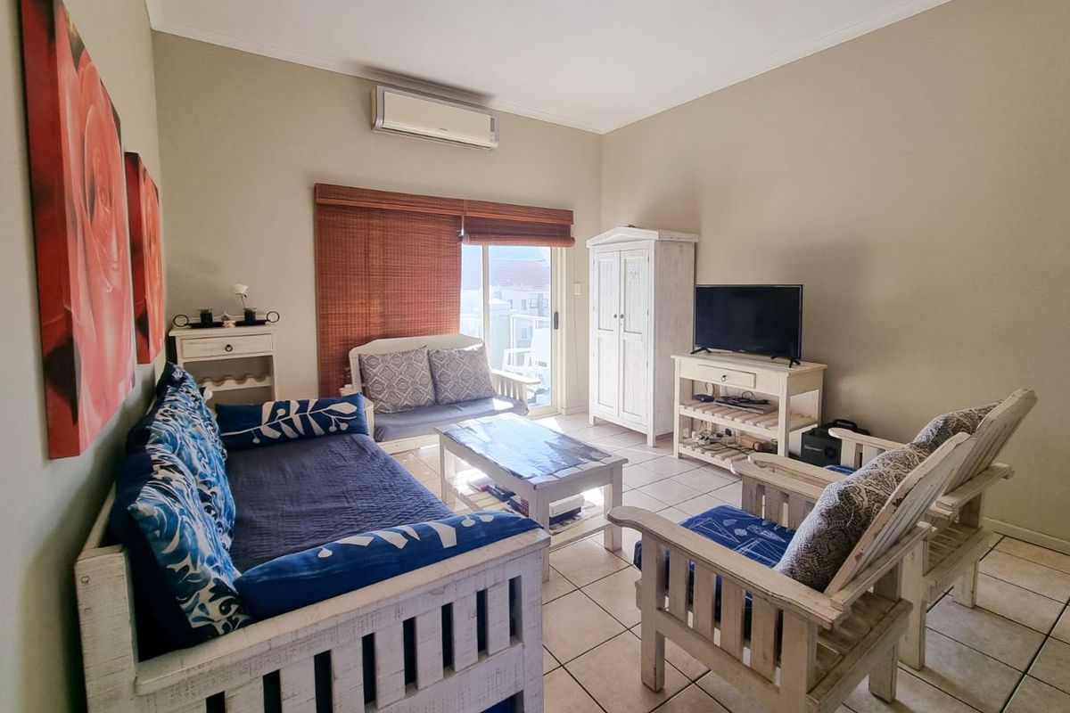 A comfortable living room featuring ceramic floor tiles, a wall-mounted air conditioning unit, and a sliding glass door providing access to the balcony.