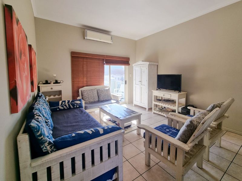 A comfortable living room featuring ceramic floor tiles, a wall-mounted air conditioning unit, and a sliding glass door providing access to the balcony.